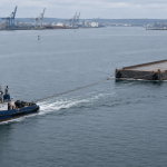 A towing tug pulling an unladen non-propelled deck barge through a harbour approach